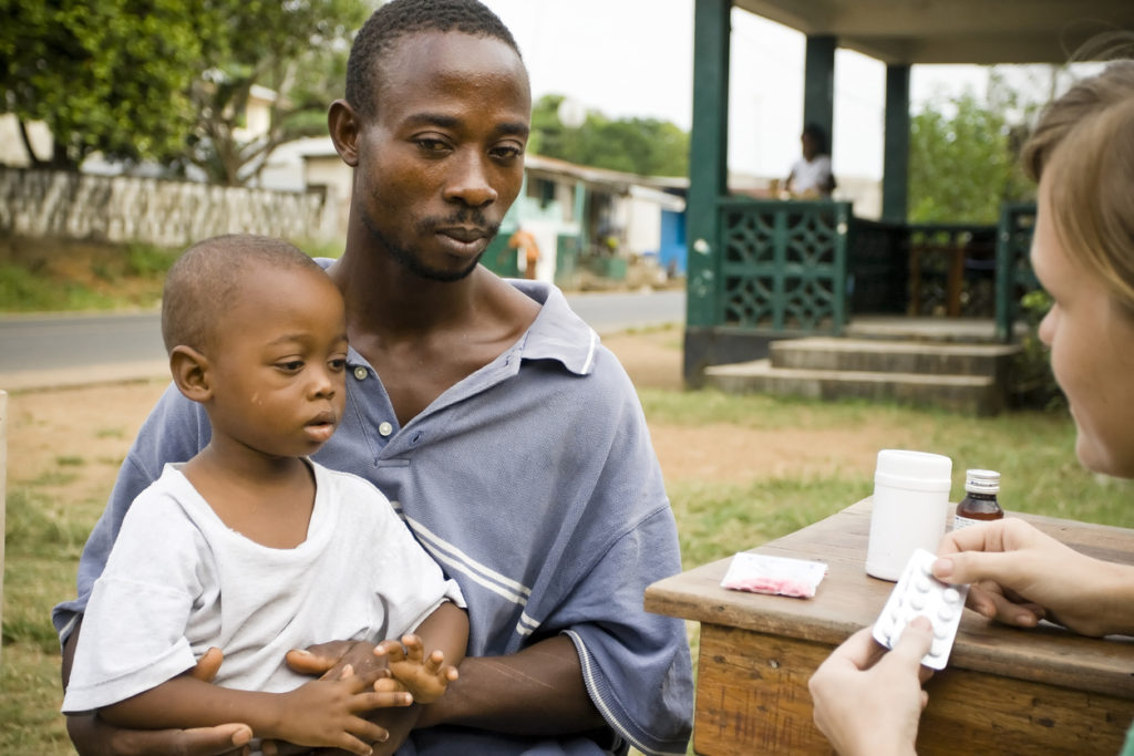 American woman explaining medication and dosage to African man holding baby son